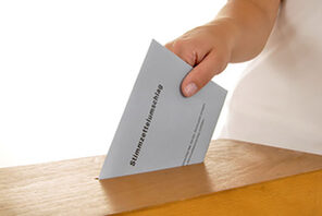 Wahlumschlag wird von einer Hand in eine Wahlurne geworfen © stock.adobe.com/Dan Race